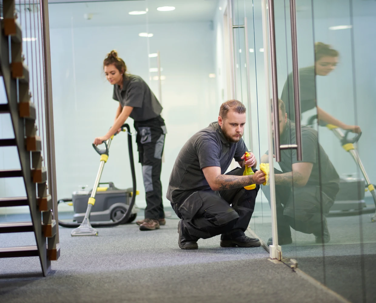 Workers cleaning glass and vacuuming carpet