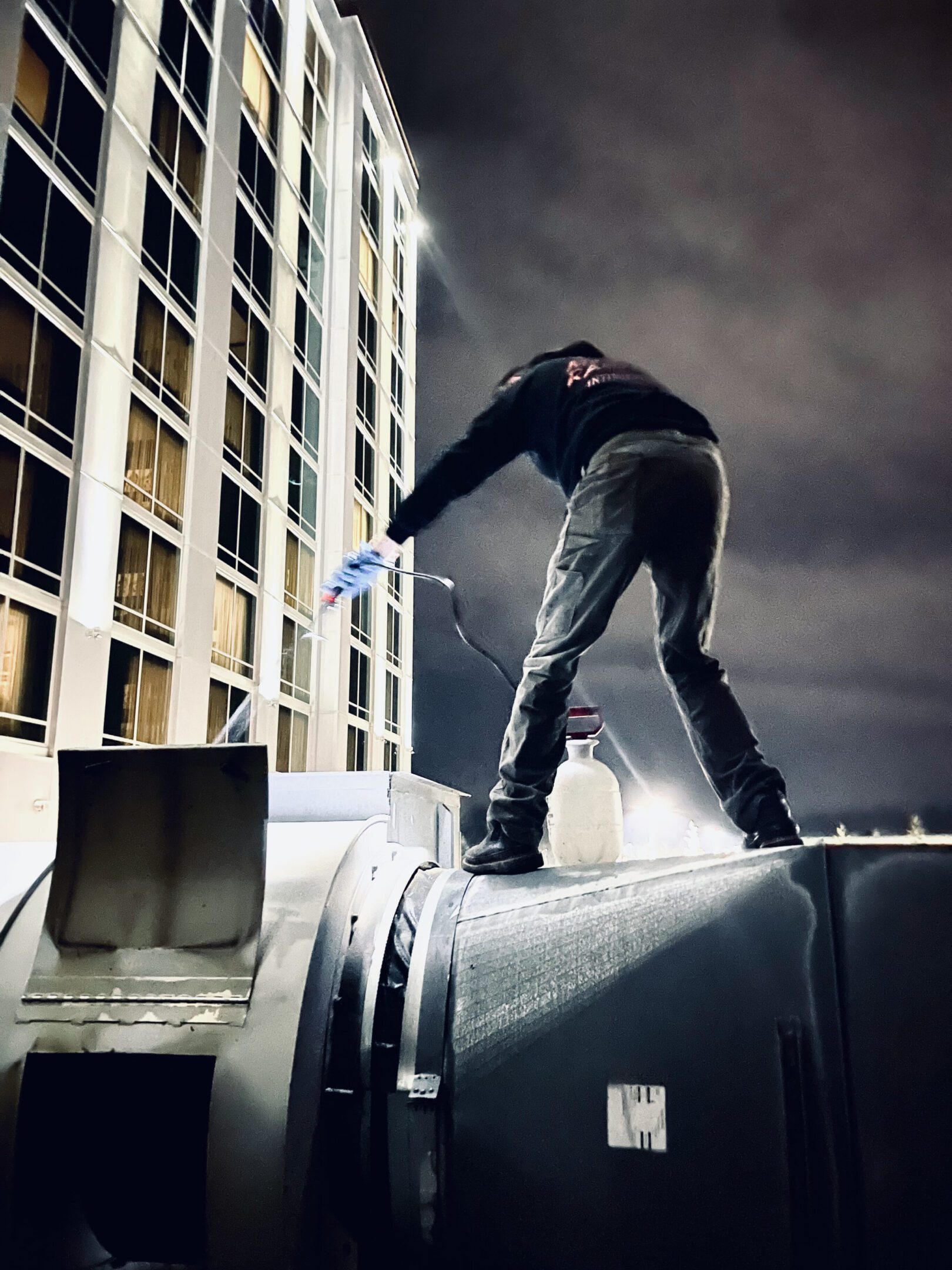 Person welding atop industrial equipment under cloudy sky.