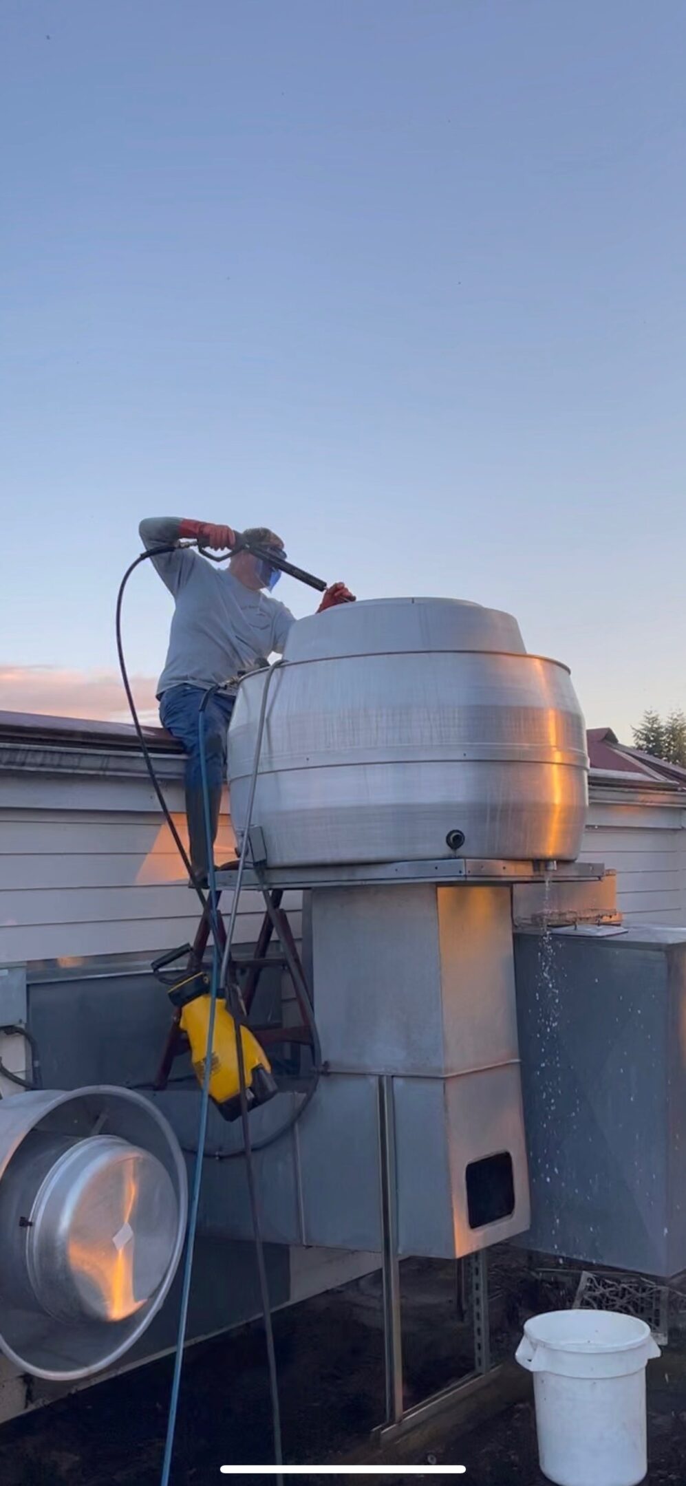 A man inspecting a large industrial fan on a rooftop at sunset.