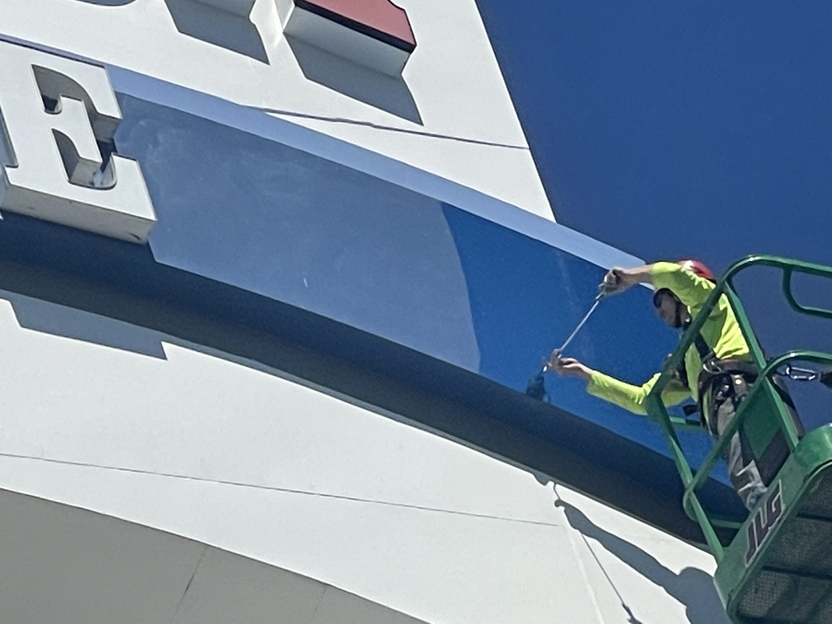 Worker in safety gear painting a tall structure under clear blue sky.
