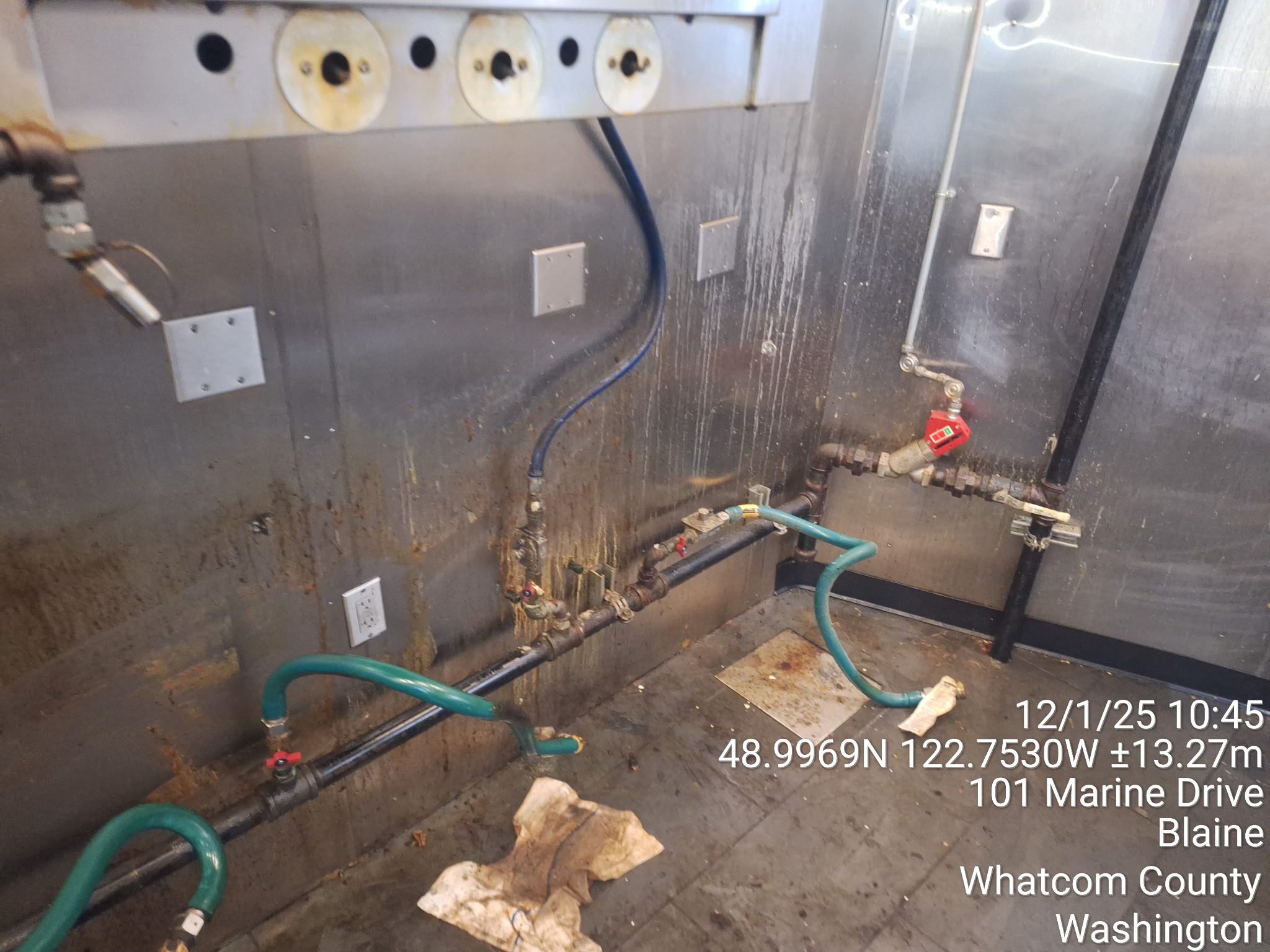 Industrial pipes and valves with gauges in a metal-paneled room.