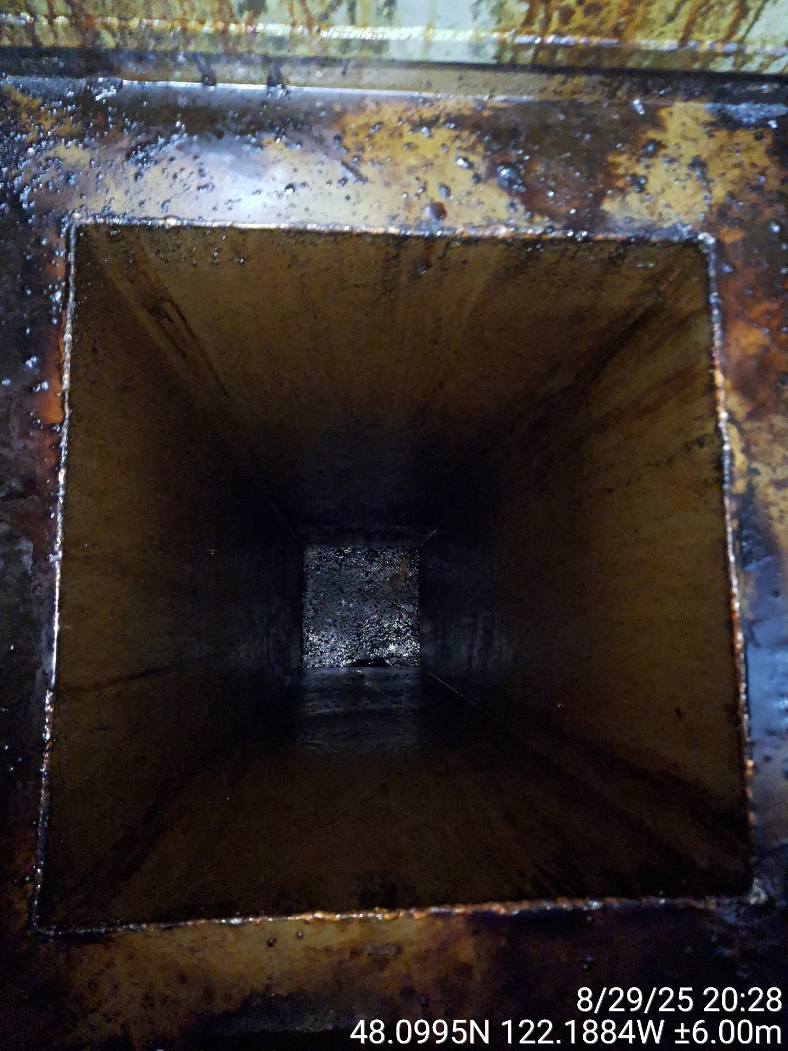 Dark, empty metallic square tunnel with rusty edges.