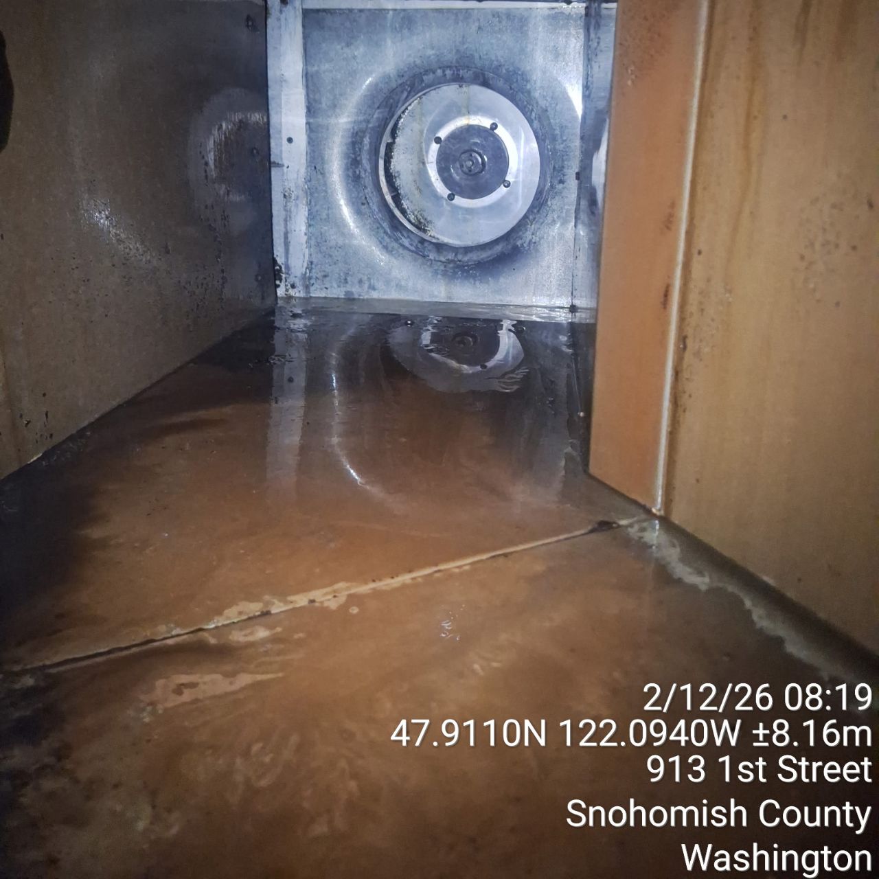 Flooded basement with water pooling on the floor and a vent on the wall.