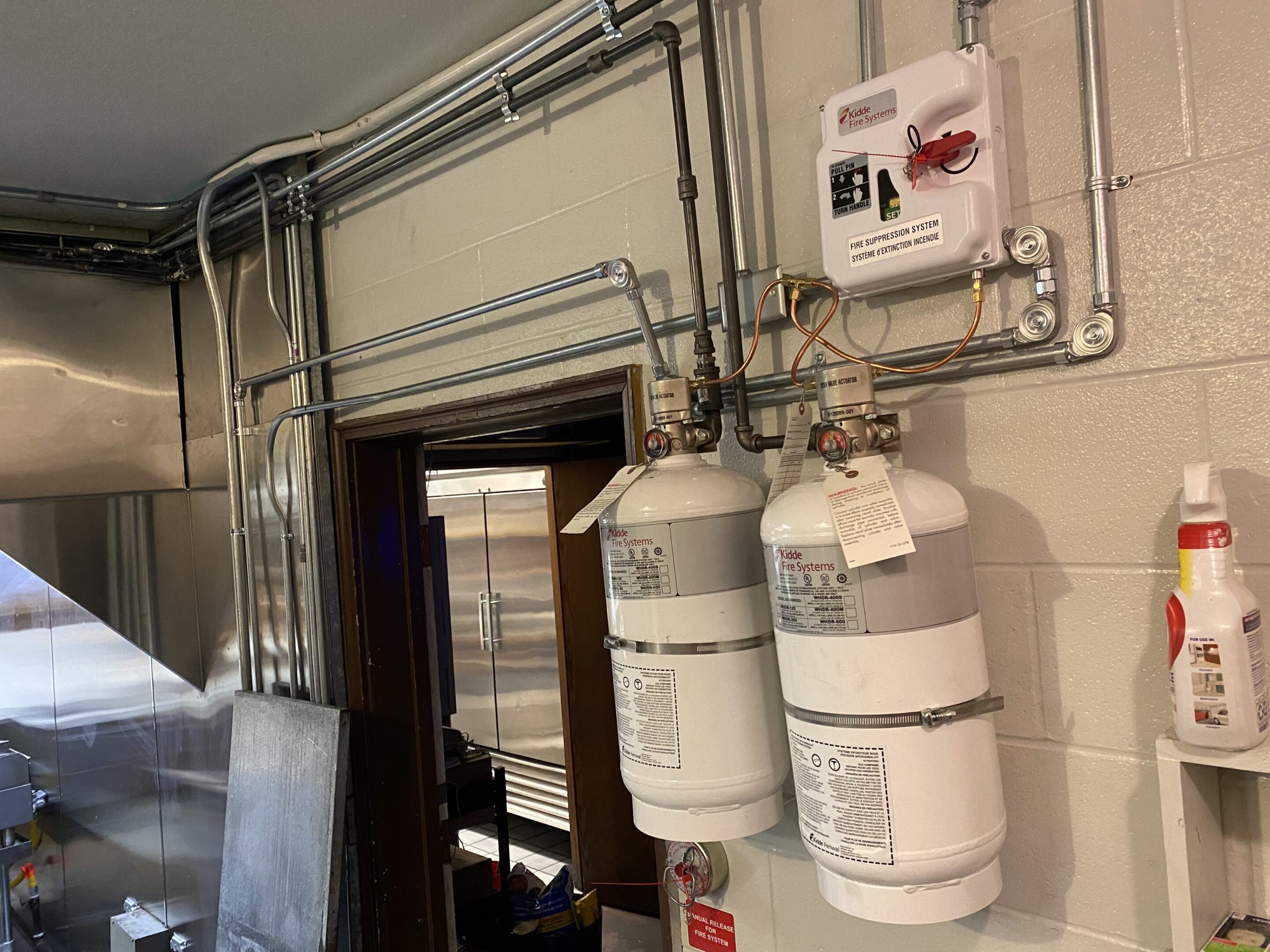 Two white fire extinguishers mounted on a wall with pipes above.