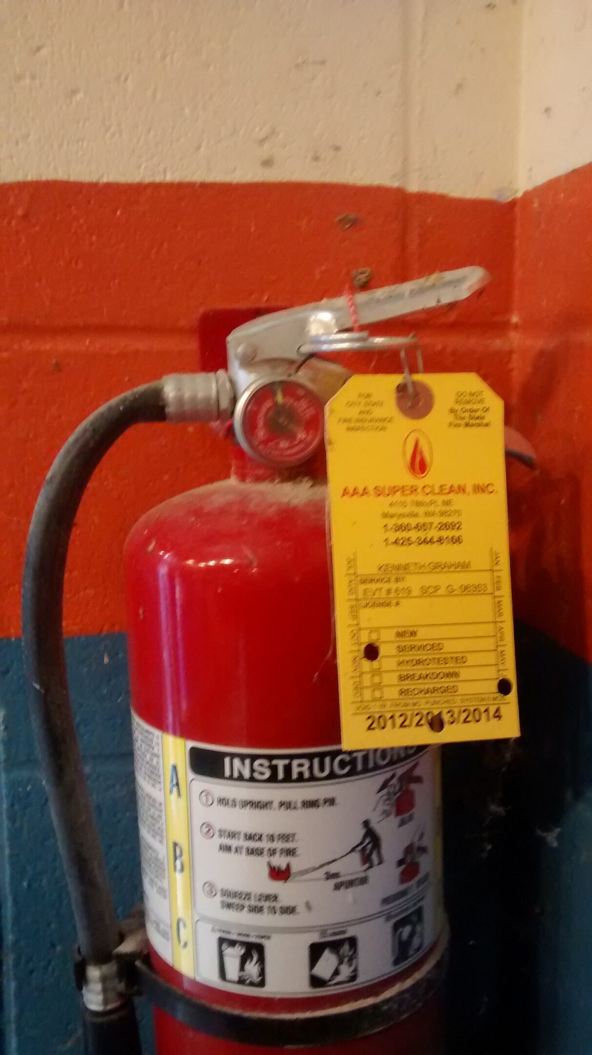 Close-up of a fire extinguisher with an inspection tag against a red background.