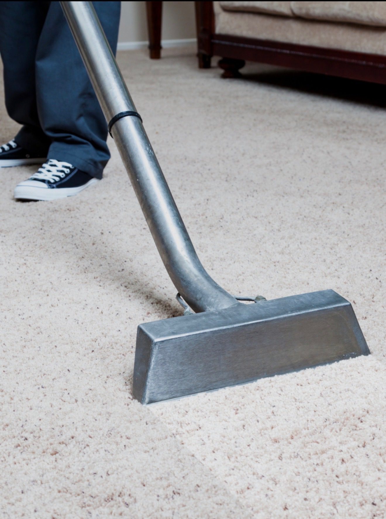 Vacuum cleaner nozzle on a carpet with a person's feet nearby.