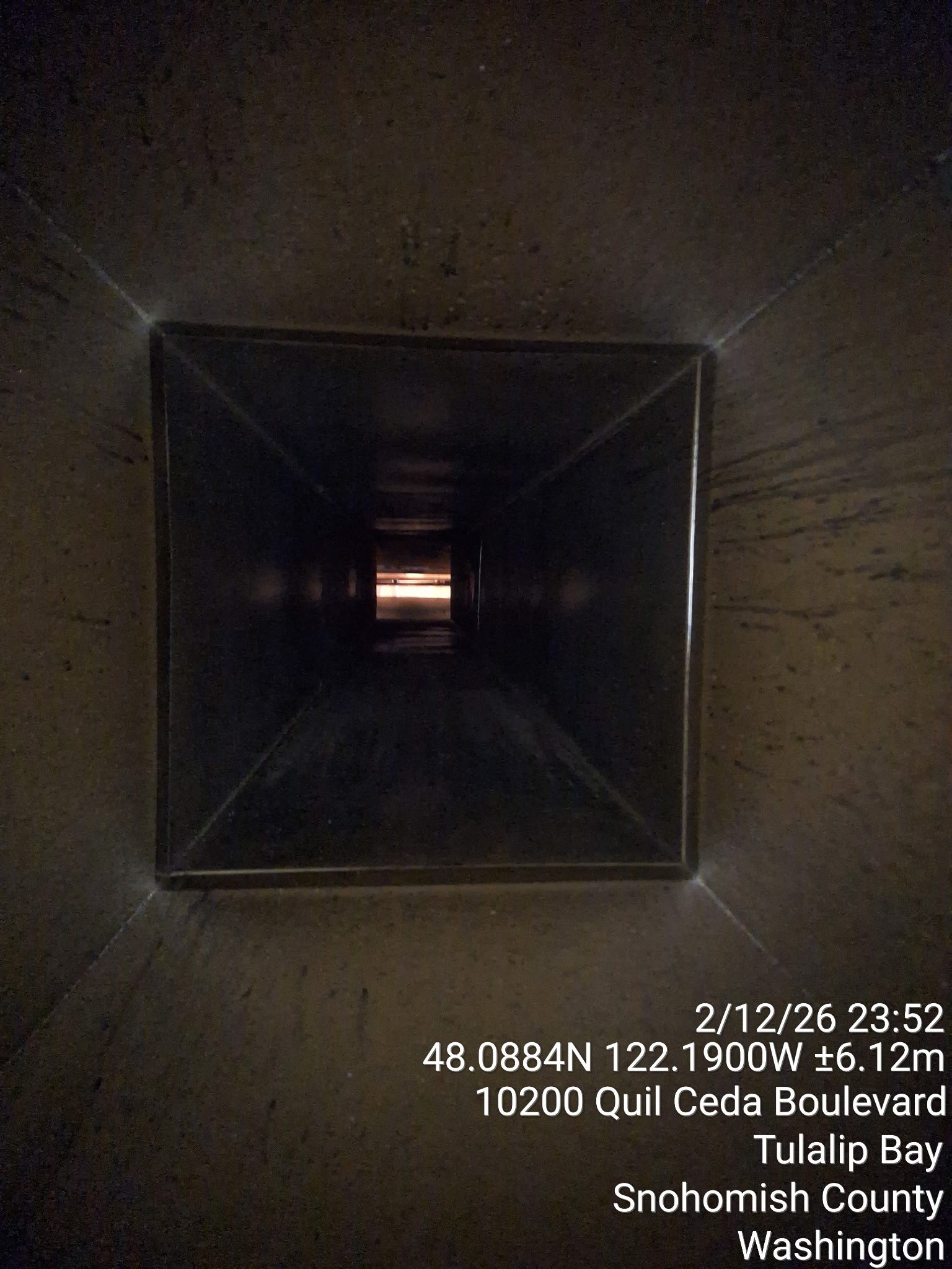 View down a long, dark, square tunnel with light at the end.
