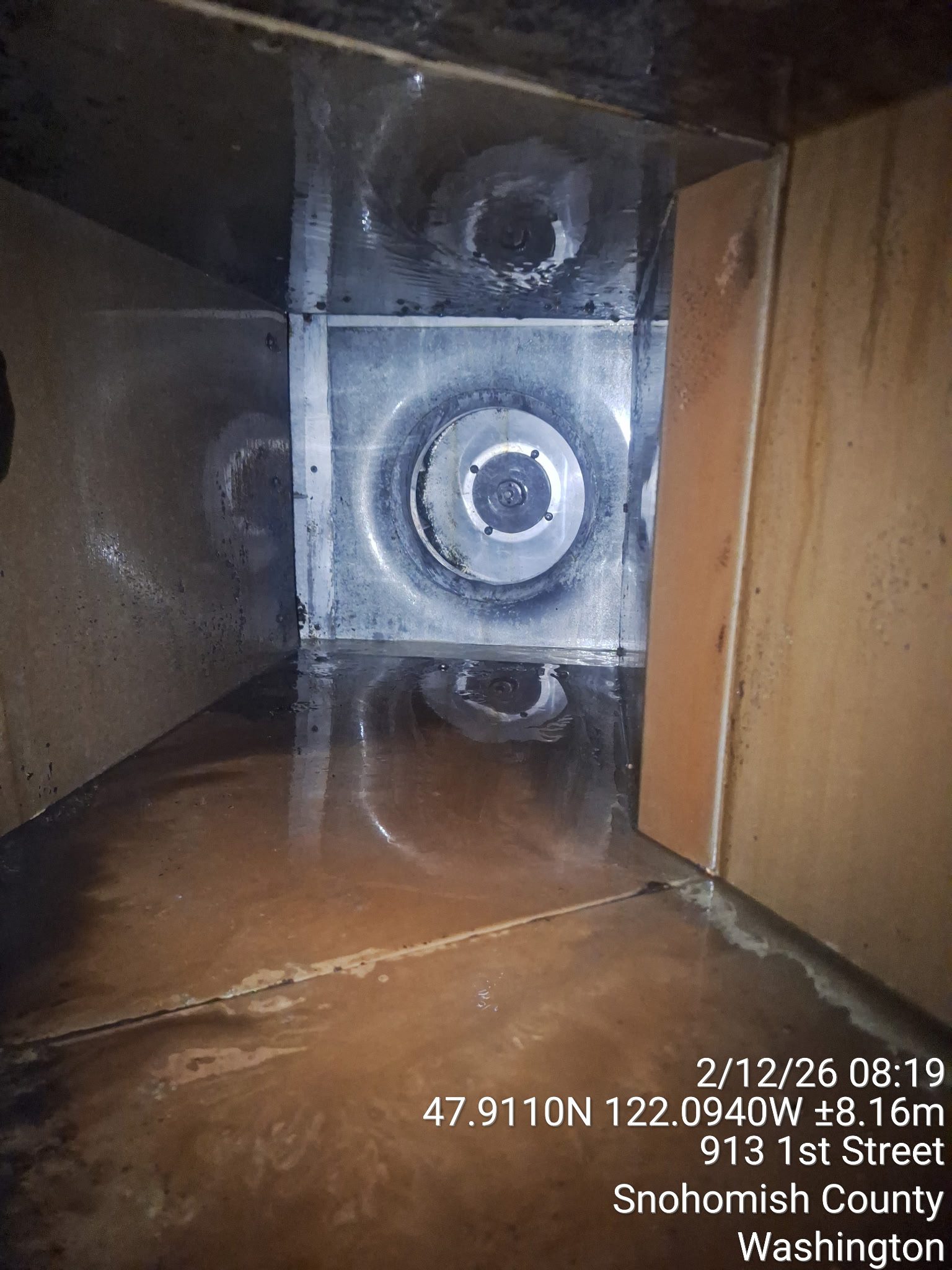 A close-up of a damaged pipe with water leakage inside a wooden cabinet.