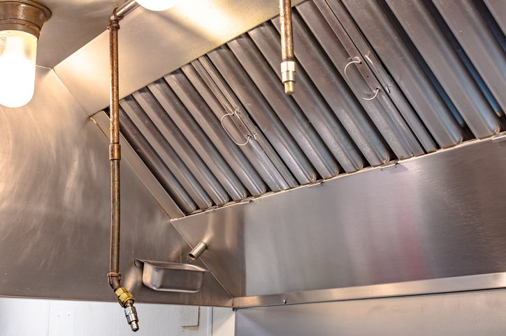 Industrial kitchen exhaust hood with hanging utensils and lighting.