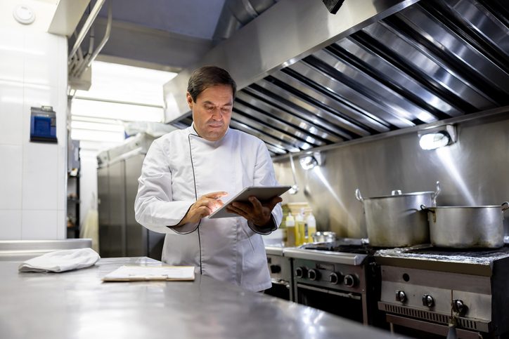 Chef reading a cookbook in a professional kitchen.