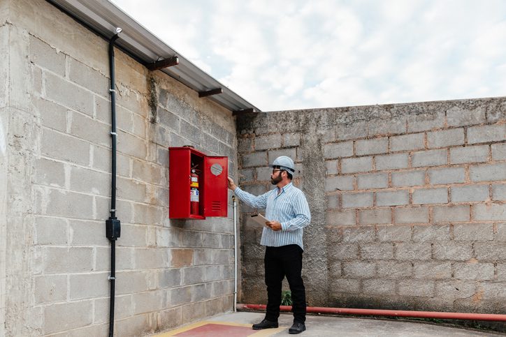Worker inspecting a fire extinguisher cabinet on a brick wall.