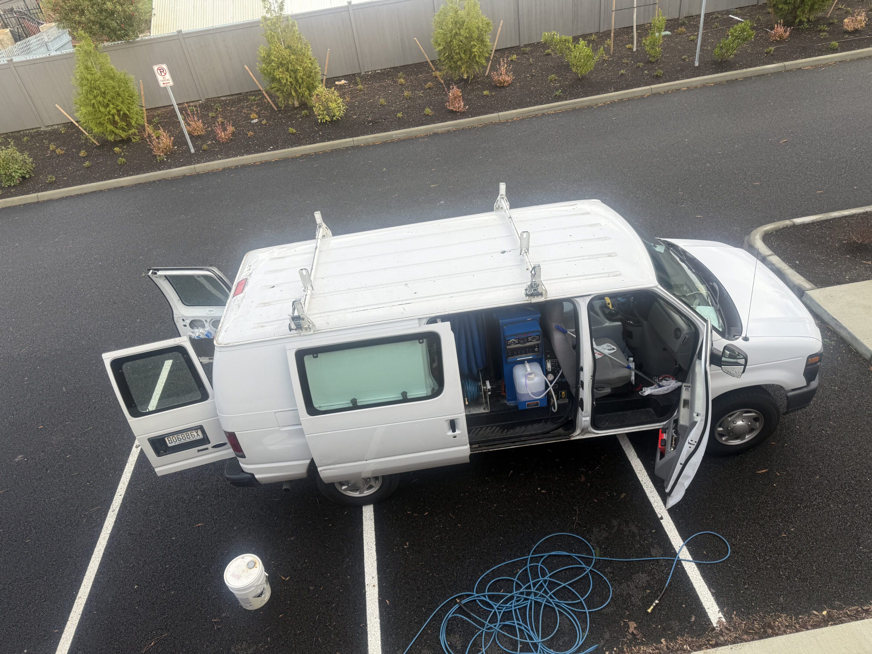 White utility van parked with open doors and equipment inside.