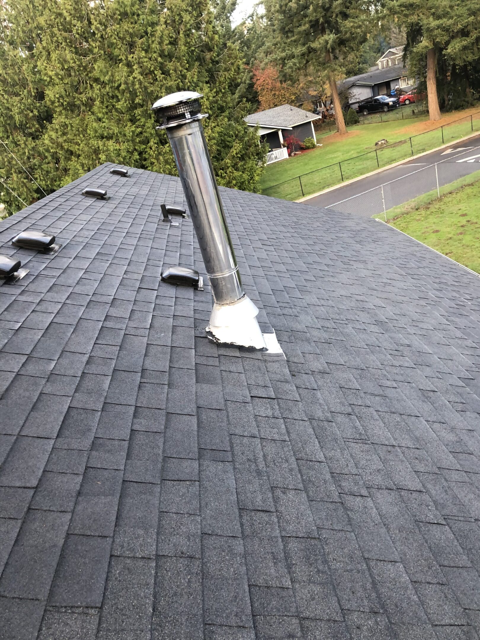 Metal chimney pipe on a shingled roof with sealant.