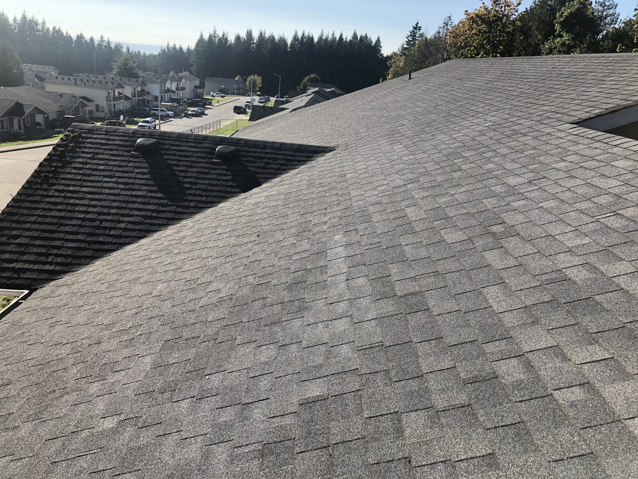 Large rooftop covered with gray shingles under a clear sky.