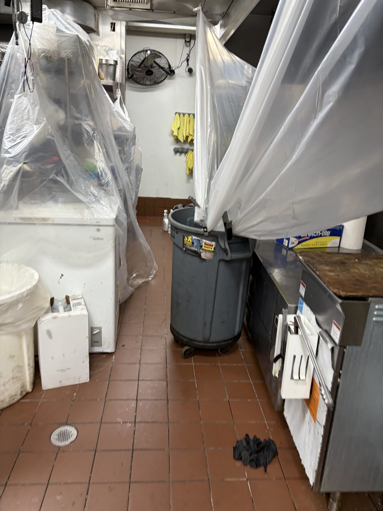 Commercial kitchen with covered equipment and storage bins.