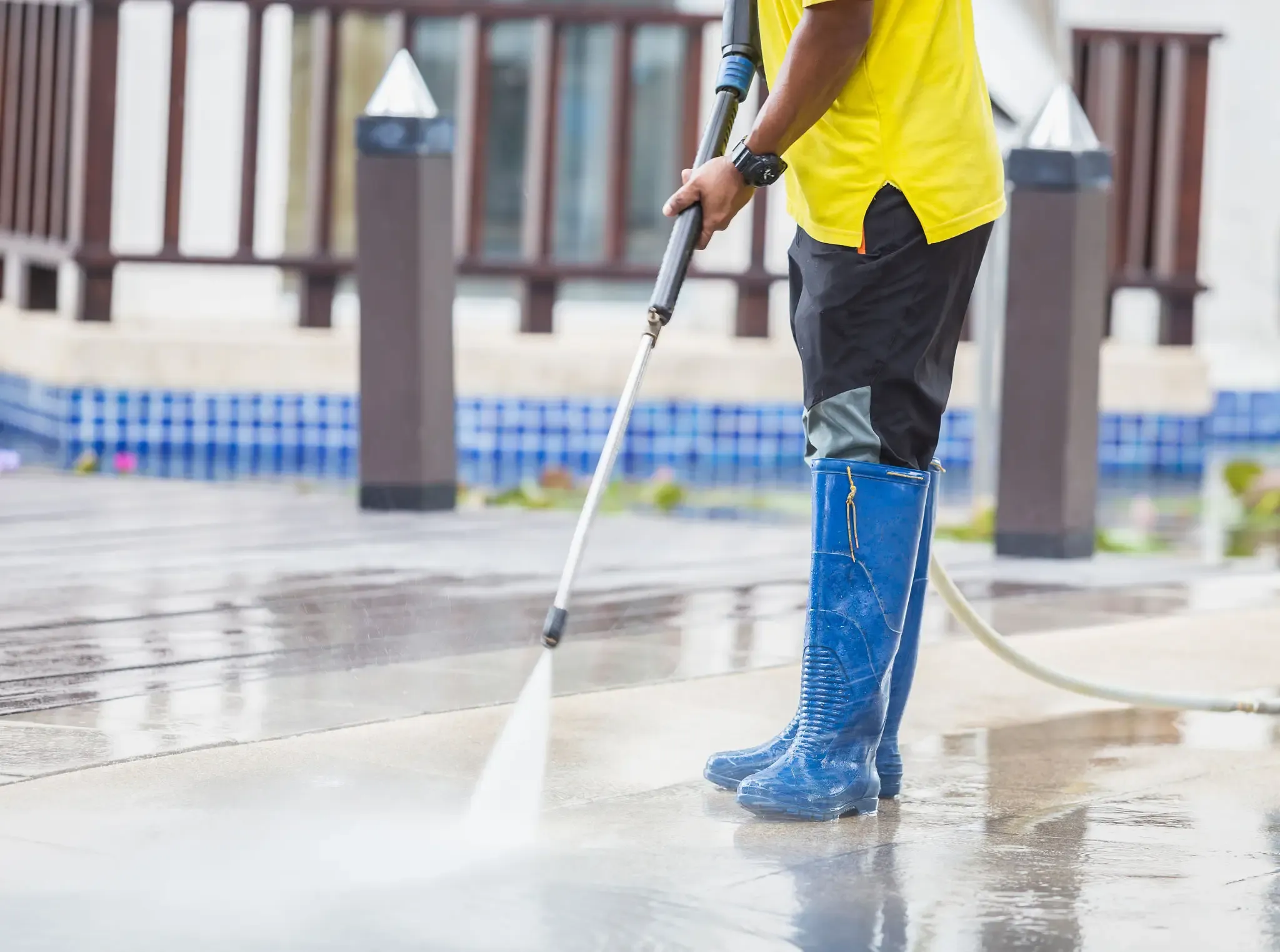 Person in blue boots pressure washing a patio.