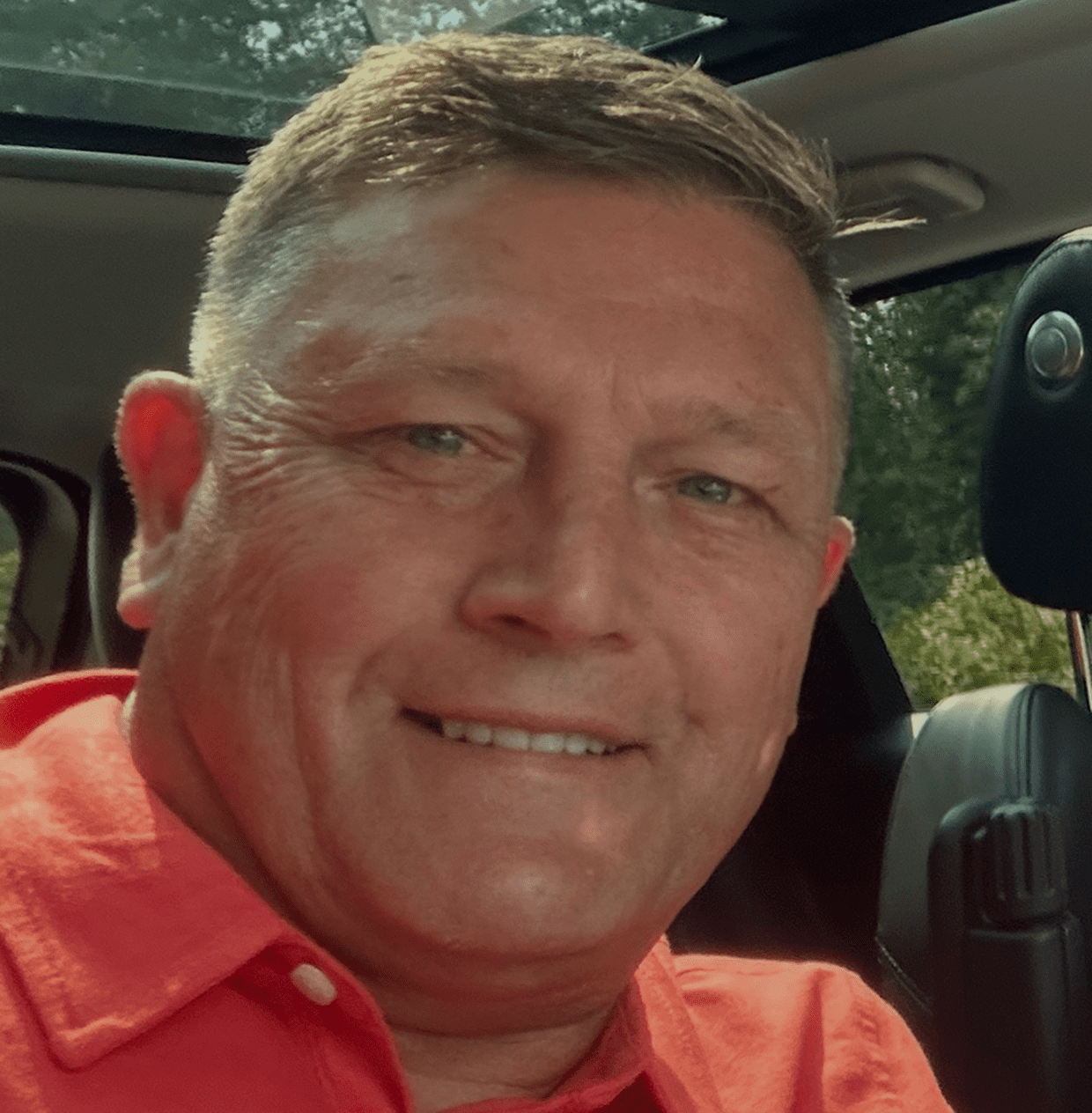 Smiling man in a red shirt sitting inside a car.
