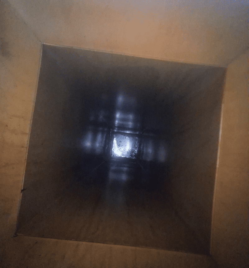 View inside a tall, dark, square-shaped tunnel or duct.