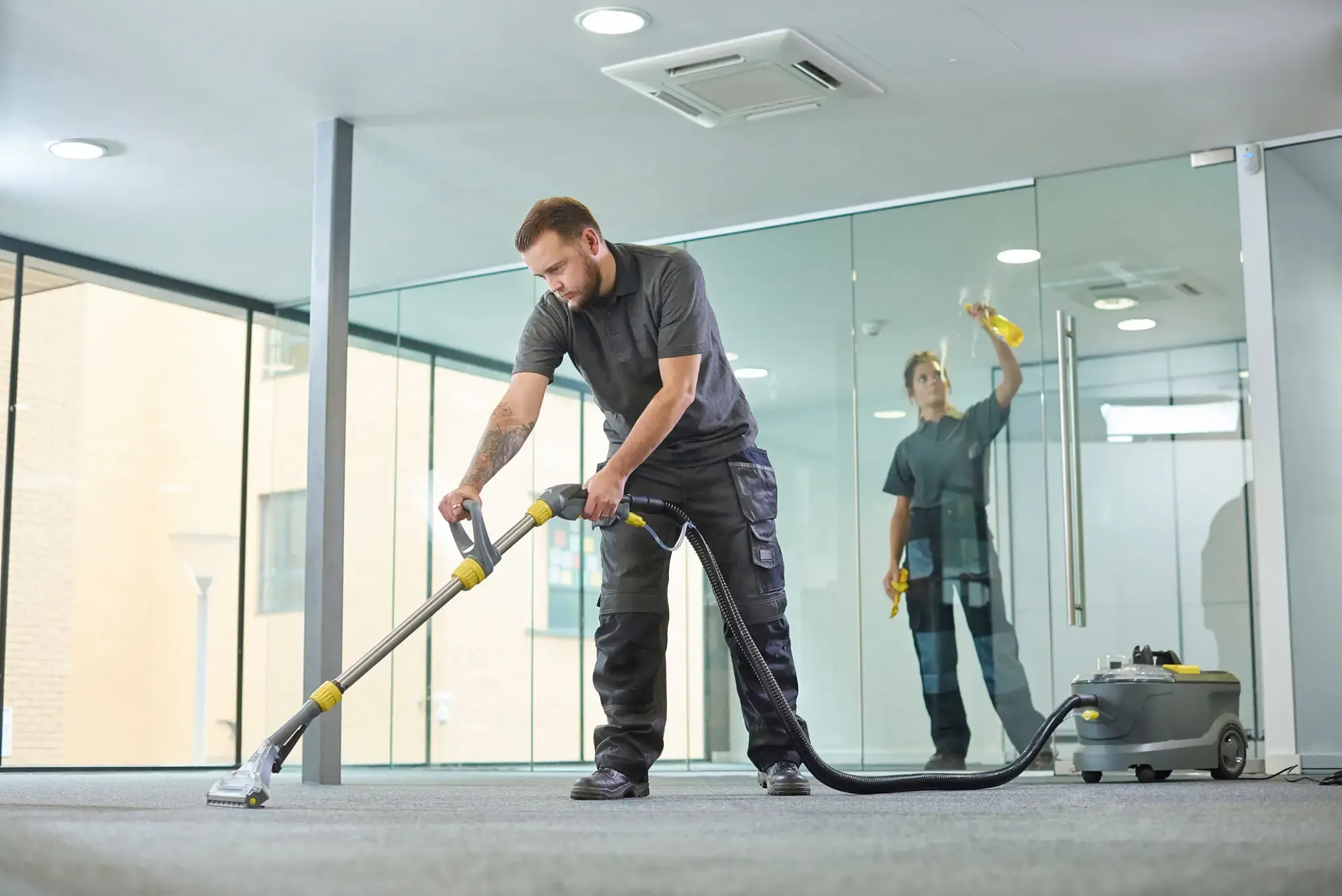 A man using a vacuum cleaner on a glass surface in a modern room.