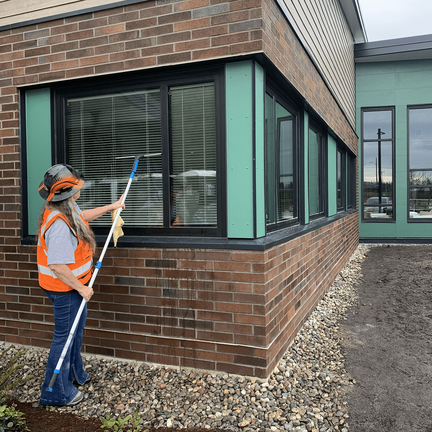 Worker cleaning windows of a brick building with a long pole.